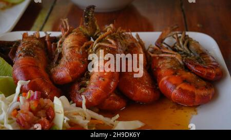 La photo montre deux plats de crevettes géantes avec sauce.Aussi sur une assiette blanche brillante est une salade de chou et une tomate.Des plats chauds sont préparés Banque D'Images