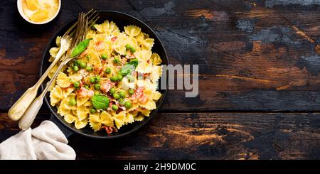 Pâtes de fettuccine au bacon et aux pois verts et au parmesan dans une vieille casserole sur fond de bois sombre.Vue de dessus. Banque D'Images