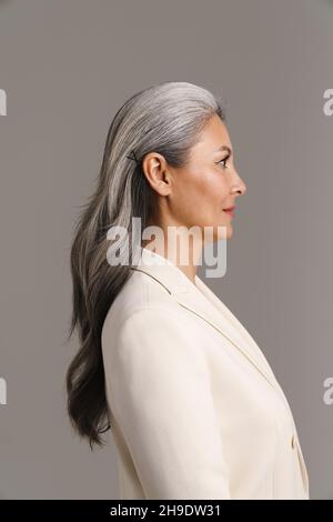 Femme asiatique mûre avec des cheveux blancs posant dans le profil isolé sur fond gris Banque D'Images