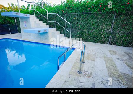 Piscine profonde de 25 mètres de long avec plongeoir.La piscine est située à l'extérieur du complexe résidentiel.Piscine au milieu de palmiers exotiques, à côté de bui blanc Banque D'Images