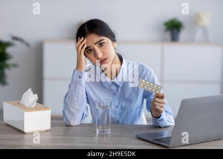 Malheureux bouleversé jeune femme indienne malade, souffrant de maux de tête, de rhumes et de grippe contient des pilules à l'intérieur du bureau Banque D'Images