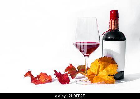 Verre à vin et bouteille avec vin rouge et feuilles de raisin d'automne sur fond blanc isolé.Concept romantique. Banque D'Images