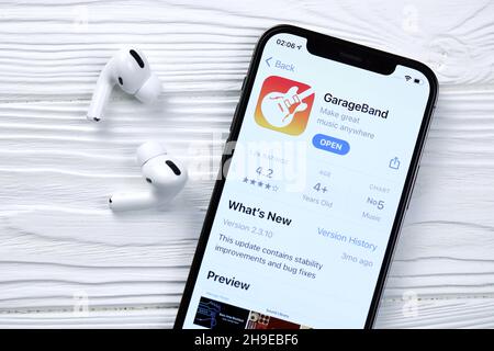 KHARKOV, UKRAINE - 5 MARS 2021 : icône GarageBand pour artistes et application de l'App Store sur iPhone 12 écran pro avec airpods pro sur blanc Banque D'Images