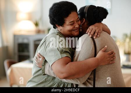 Portrait d'une femme afro-américaine senior qui embrasse sa fille et souriant tout en accueillant les invités pour dîner à la maison Banque D'Images