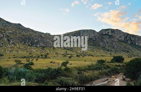 Prairies vertes avec rochers, quelques arbres, falaises rocheuses abruptes arrière-plan, rivière coulant en premier plan, paysage typique de Madagascar dans la région près de Zazafots Banque D'Images