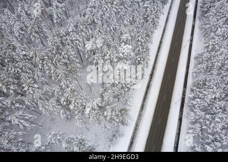 Vue aérienne de la route asphaltée menant à travers des forêts hivernales gelées et des bosquets couverts de givre et de neige.Photo de drone de la route noire et des arbres avec de la neige fraîche dans les montagnes.Thème de Noël Banque D'Images