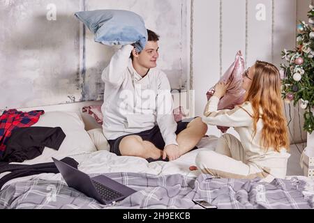 Bataille d'oreillers de jeunes couples assis sur le lit dans leur chambre. Banque D'Images