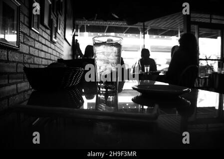 Image en noir et blanc d'un verre d'eau et d'une table dans un restaurant.Arrière-plan de mise au point douce. Banque D'Images