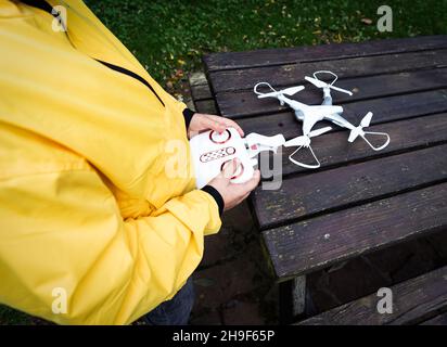 Petit garçon caucasien dans un manteau jaune essayant d'actionner un drone dans le parc par une journée ensoleillée Banque D'Images