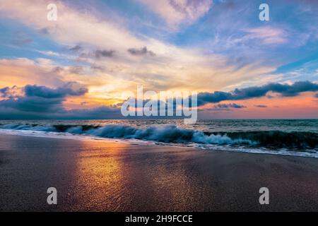 Un magnifique coucher de soleil coloré sur l'océan tandis Qu'Une vague s'écrase sur la Sandy Shore Banque D'Images