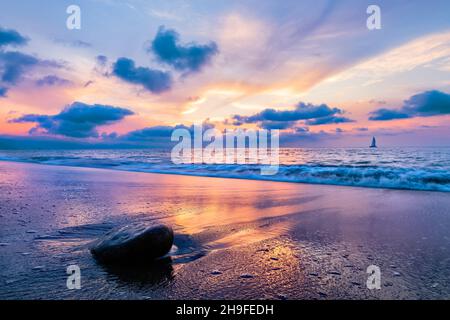 Un magnifique coucher de soleil coloré sur l'océan tandis Qu'Une vague s'écrase sur la Sandy Shore Banque D'Images