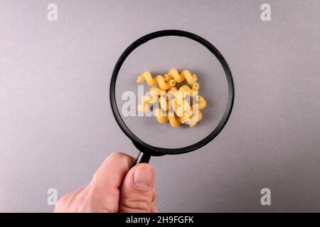 Pâtes Cavatappi Macaroni.Homme tenant une loupe sur fond gris. Banque D'Images