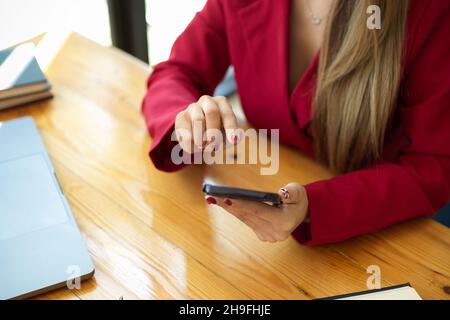 Image rapprochée d'une femme d'affaires élégante utilisant un smartphone pour communiquer avec ses partenaires au bureau. Banque D'Images
