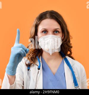 Le médecin fait un doigt prudent - mouvement vers le haut, espace de copie.Une femme en gants de protection médicale et un masque sur fond rouge, concept Banque D'Images