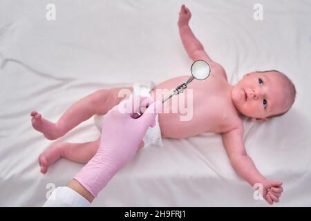 Un médecin en uniforme vérifie la bouche d'un enfant avec un miroir. Le dentiste examine les dents d'un nouveau-né Banque D'Images