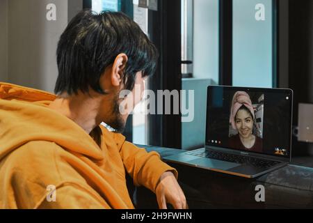 Un homme asiatique s'assied dans un petit bureau et communique par liaison vidéo via un ordinateur portable avec sa petite amie.Le concept de communication en ligne, quarant Banque D'Images