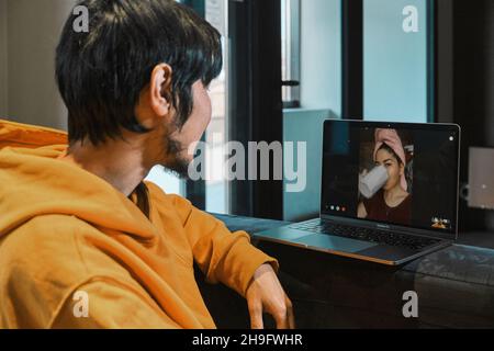 Un homme asiatique s'assied dans un petit bureau et communique par liaison vidéo via un ordinateur portable avec sa petite amie.Le concept de communication en ligne, quarant Banque D'Images
