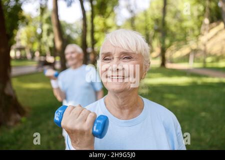 Bonne dame senior fait des exercices avec entraînement de haltères avec partenaire dans le parc Banque D'Images