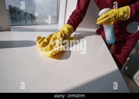 Travailleur en gants de caoutchouc nettoyant le seuil avec un chiffon en microfibre Banque D'Images