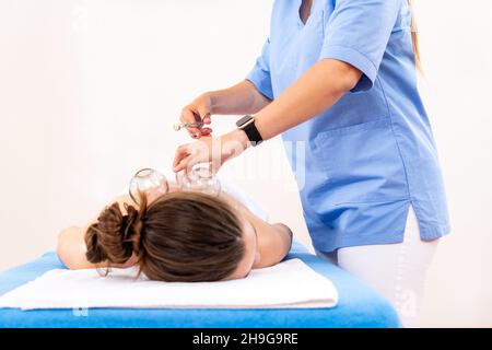 Arrière-plan de la cupthérapie sous vide.Une jeune physiothérapeute femme applique des ventouses sur le dos de sa patiente, pour soulager les douleurs musculaires. Banque D'Images