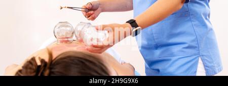 Bannière pour la cupthérapie sous vide.Une jeune physiothérapeute femme applique des ventouses sur le dos de sa patiente, pour soulager les douleurs musculaires. Banque D'Images