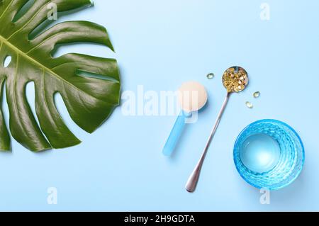 Poudre de collagène et capsules de gélatine jaune, verre d'eau pure sur fond bleu.Concept sain et anti-âge.Flat lay, vue de dessus Banque D'Images