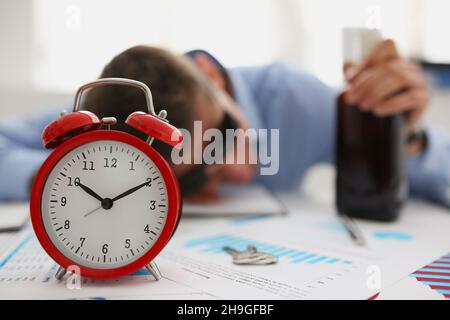 Rouge vintage horloge montre l'heure, homme ivre s'est endormi sur le lieu de travail dans le bureau Banque D'Images