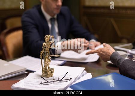 Statue de justice et lunettes sur une pile de documents juridiques sur la table où deux avocats discutent de documents Banque D'Images