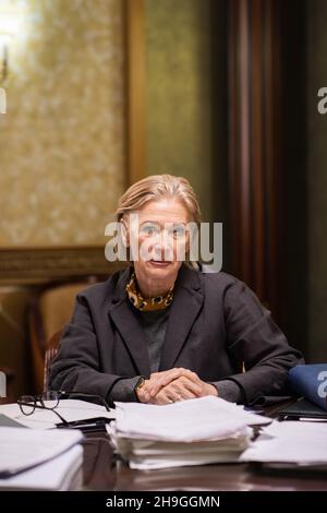 Femme avocate fiable et mature qui vous regarde tout en étant assise sur le lieu de travail avec des piles de documents juridiques Banque D'Images