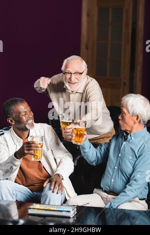 un homme senior heureux montrant un geste de victoire tout en regardant le championnat de football avec des amis interraciaux Banque D'Images