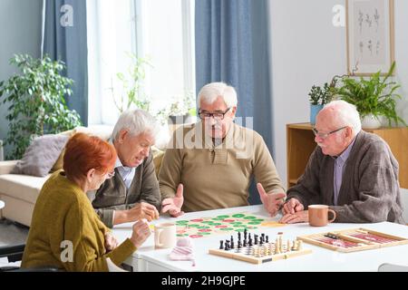Groupe de personnes âgées assis à la table et jouant au jeu de société dans la chambre Banque D'Images