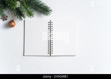 Vue de dessus des décorations de Noël arrière-plan avec bloc-notes vierge sur fond de table blanc avec espace de copie, concept de fête de vacances. Banque D'Images