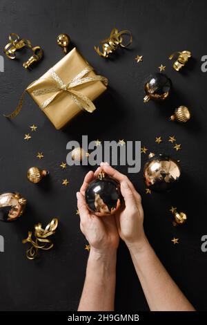 Boules noires décorées or métallisé pot dans les mains de femme et cadeau d'or pour les vacances de Noël.Carte de vœux verticale de Noël ou invitation au nouvel an p Banque D'Images