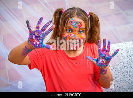 La fillette heureuse a été enduite de peinture.Un enfant aux couleurs vives sur son visage, ses mains et ses cheveux sourit Banque D'Images