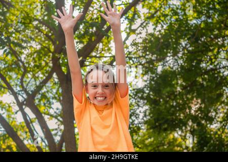 l'enfant aime la vie, sourit et lève les mains sur le fond des arbres. Banque D'Images