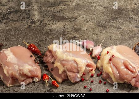 Cuisse de poulet crue sans os ni peau.Un ingrédient utile pour préparer des aliments sains, des épices, de l'ail.Arrière-plan en pierre sombre, espace de copie Banque D'Images