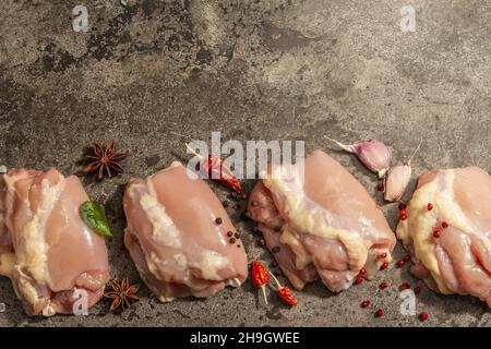 Cuisse de poulet crue sans os ni peau.Un ingrédient utile pour préparer des aliments sains, des épices, de l'ail.Arrière-plan en pierre sombre, vue du dessus Banque D'Images