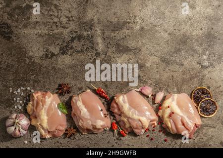 Cuisse de poulet crue sans os ni peau.Un ingrédient utile pour préparer des aliments sains, des épices, de l'ail.Arrière-plan en pierre sombre, vue du dessus Banque D'Images