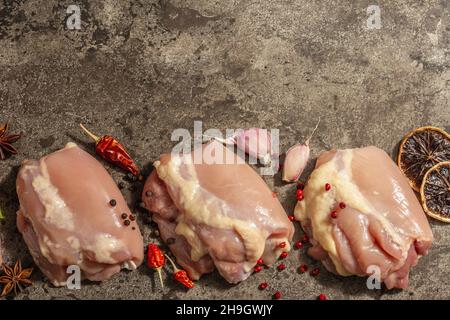 Cuisse de poulet crue sans os ni peau.Un ingrédient utile pour préparer des aliments sains, des épices, de l'ail.Arrière-plan en pierre sombre, vue du dessus Banque D'Images