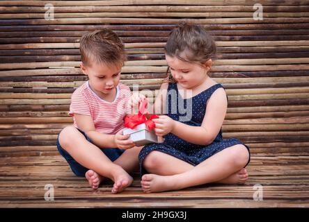 les enfants ouvrent une boîte cadeau. garçon tient la boîte blanche et fille tire l'arc rouge Banque D'Images