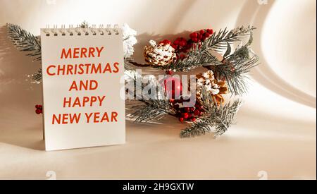 Texte JOYEUX NOËL ET BONNE ANNÉE sur un bloc-notes avec des décorations d'arbre de Noël sur un fond blanc.Joyeux Noël et bonne année greeti Banque D'Images