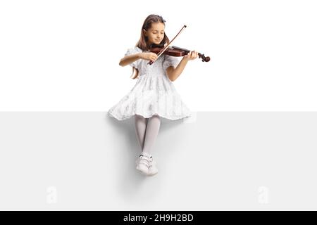 Portrait d'une fille en robe blanche assise sur un panneau vierge et jouant un violon isolé sur fond blanc Banque D'Images