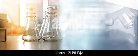 flacon transparent et livre de texte avec microscope dans le laboratoire des sciences de la santé formation bannière fond Banque D'Images