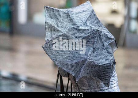 Vents forts et femme portant un parapluie rose inversé à Preston, parapluie brisé, inversé, endommagé, piquant lors d'un jour de pluie à Lancashire, Royaume-Uni.Décembre 2021.Météo britannique, parapluie cassé, inversé, intérieur vers l'extérieur, plié cassé par le vent et la pluie.Magasins, shopping shopping lors d'une journée humide et venteuse dans le centre-ville de Preston.Crédit : MediaWorlImages/AlamyLiveNews Banque D'Images