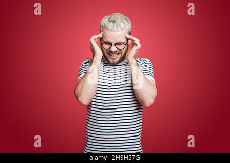 Portrait d'un homme appuyant les doigts sur les temples, fermant les yeux.Portrait d'un homme portant des lunettes isolées sur fond rouge souffrant de graves Banque D'Images