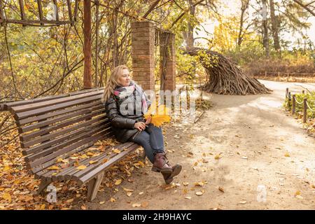 Portrait d'une femme assise sur un banc dans un belvédère entouré d'une vigne dans un parc d'automne. Banque D'Images