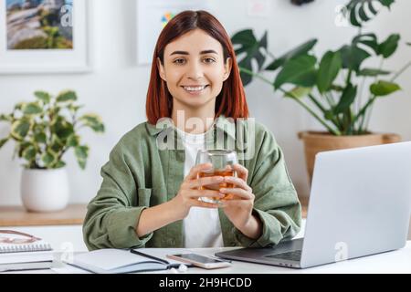 Portrait d'une jeune femme travaillant à la maison avec un ordinateur portable.Femme d'affaires décontractée tenant une tasse de thé.Concept d'affaires ou de communication en ligne, freelance, Banque D'Images