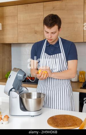 Jeune homme beau en tablier pétriant la pâte dans la cuisine moderne.Concept de boulangerie maison, cuisine masculine et style de vie domestique.Pâtisserie du chef Banque D'Images