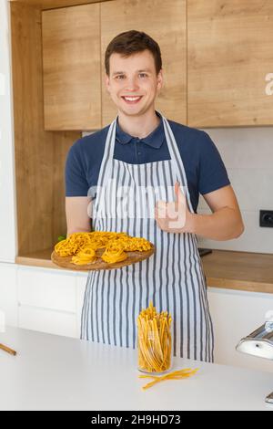 Jeune homme beau dans un plateau de maintien avec des nouilles de pâtes crues.Concept de boulangerie maison, cuisine masculine et style de vie domestique.Le chef ne fait pas Banque D'Images