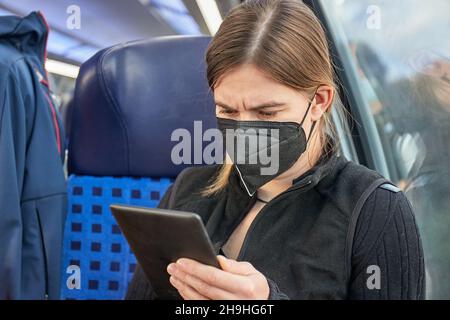 Femme dans un train portant un masque et lisant Banque D'Images